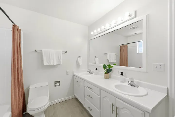 Dual vanity with integrated sinks, white cabinetry, a large framed mirror, and wood-finish flooring