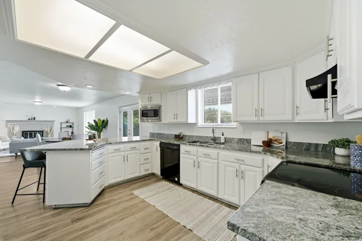 Kitchen featuring white cabinetry, granite countertops, a built-in microwave, black appliances, and wood-finish flooring