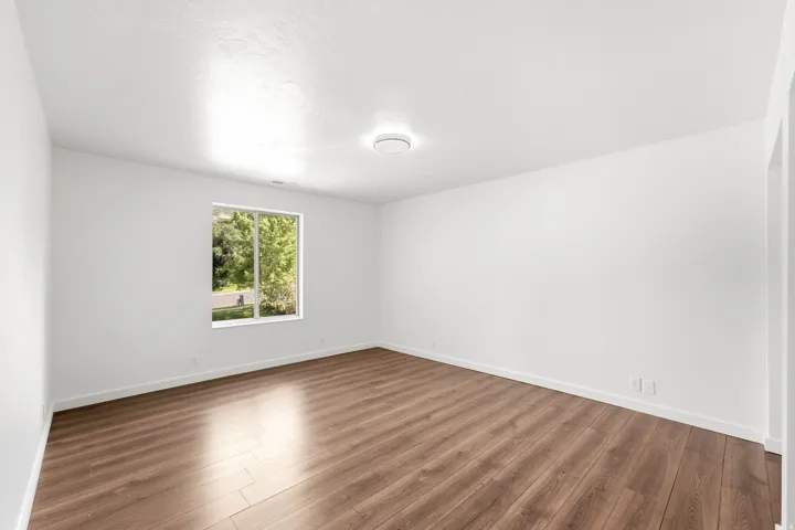 Expansive room featuring wood-finish flooring, white walls, a large window, and a flush-mount ceiling light
