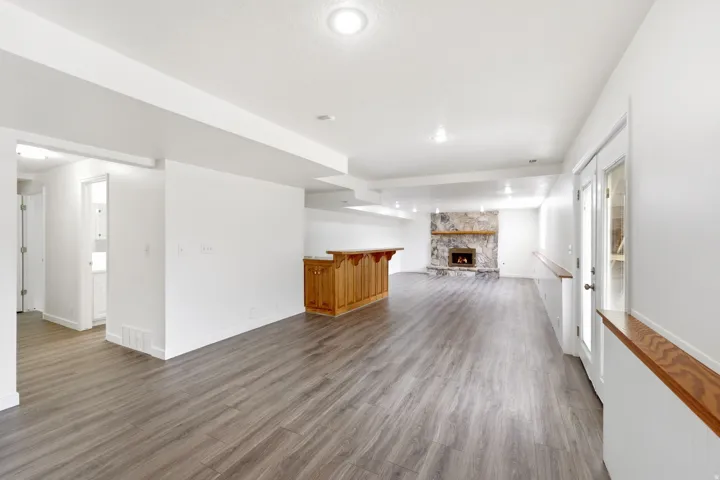 Expansive room featuring wood-finish flooring, a stone-clad fireplace, and a built-in wood bar