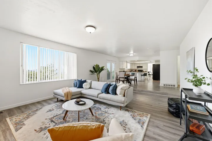 Spacious living area featuring wood-finish flooring, a large window with vertical blinds, and a built-in ceiling light