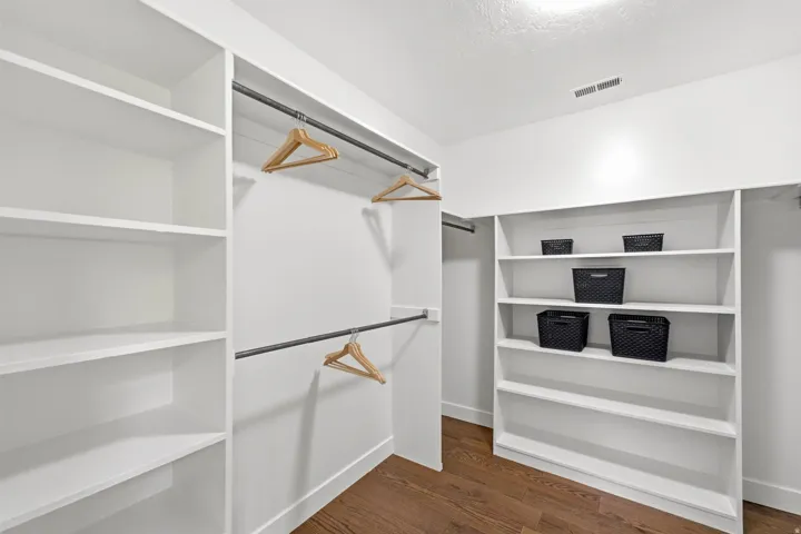 Walk-in closet with integrated white shelving, dual hanging rods, and wood-finish flooring