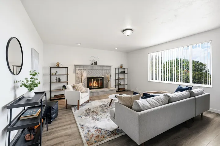 Living area featuring wood-finish flooring, a brick fireplace with a chevron pattern, recessed lighting, and a large window with vertical blinds