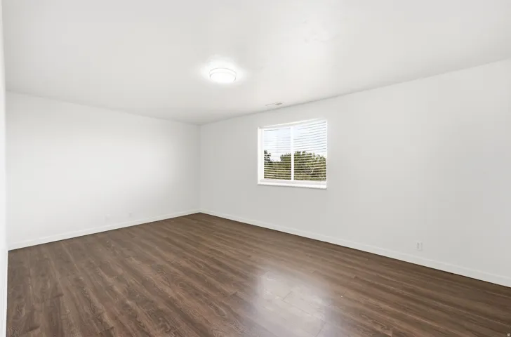 Room featuring wood-finish flooring, white walls, and a single window with horizontal blinds