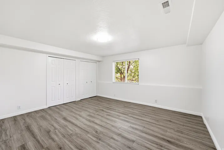 Wood-finish flooring, white walls, two bi-fold door closets, and a window with blinds