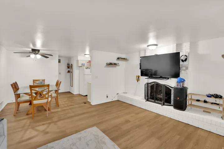 Open-concept living space with wood-finish flooring, a white brick fireplace, and a ceiling fan