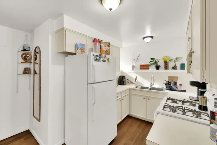 Kitchen featuring wood-finish flooring, white cabinetry, solid surface countertops, and a double basin sink with a gooseneck faucet