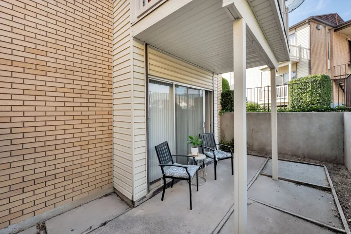 Covered patio with concrete flooring, supported by two white columns, featuring a sliding glass door entry