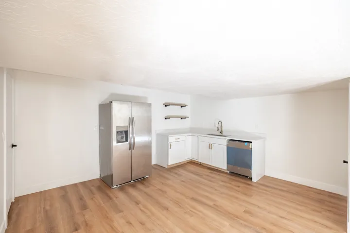 Wood-finish flooring, white cabinetry, light-toned countertops, stainless steel appliances, and floating wood shelves