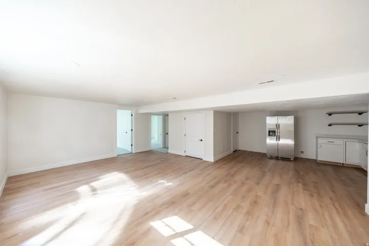 Expansive room featuring wood-finish flooring, white walls, and a stainless steel refrigerator