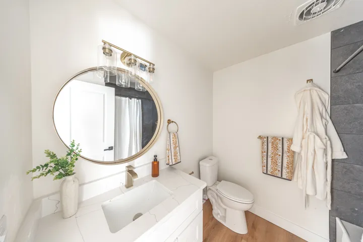 White vanity with a rectangular undermount sink, brass-finish faucet, and coordinating circular mirror