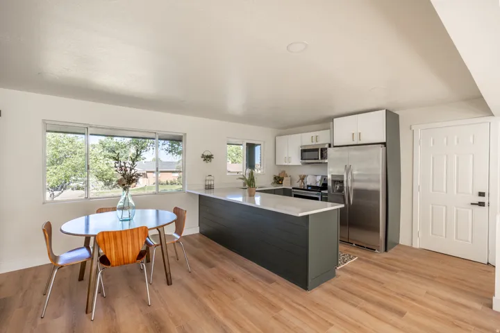 Open-concept kitchen and dining area featuring wood-finish flooring, white cabinetry, stainless steel appliances, and a central island with a light-colored countertop