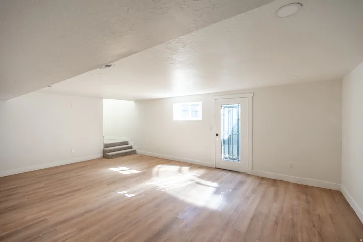Spacious room featuring wood-finish flooring, recessed lighting, and a white paneled door with decorative glass