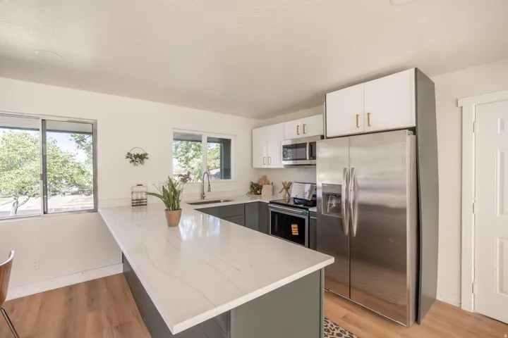 Kitchen featuring a spacious island with a light-toned countertop, stainless steel appliances, white upper cabinetry, and wood-finish flooring