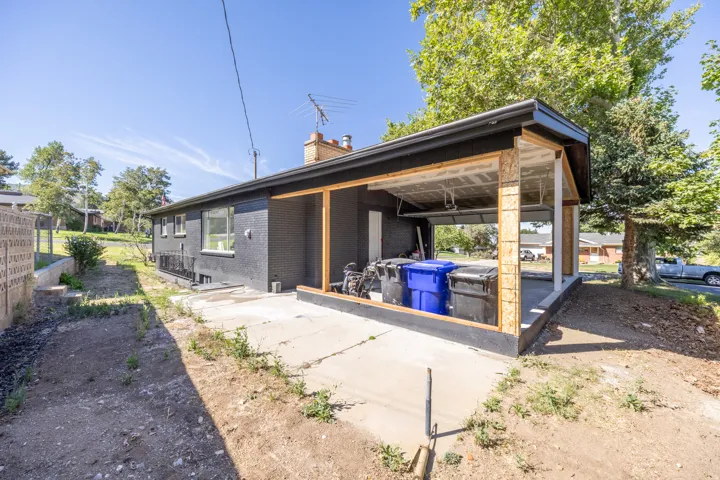 Carport structure with unfinished wood framing, black exterior siding, and a concrete pad