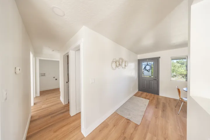 Wood-finish flooring throughout, white walls, recessed ceiling lighting, and a gray front door with an integrated glass panel