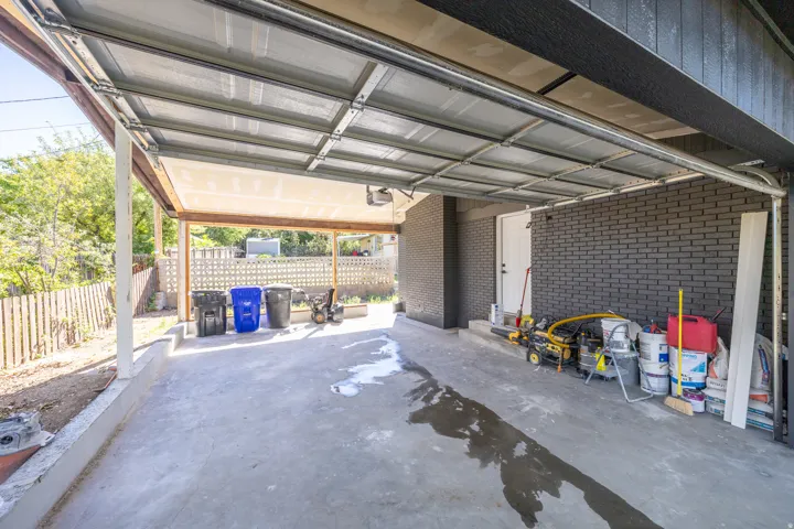 Carport with concrete flooring, exposed wood beam framing, and a white access door