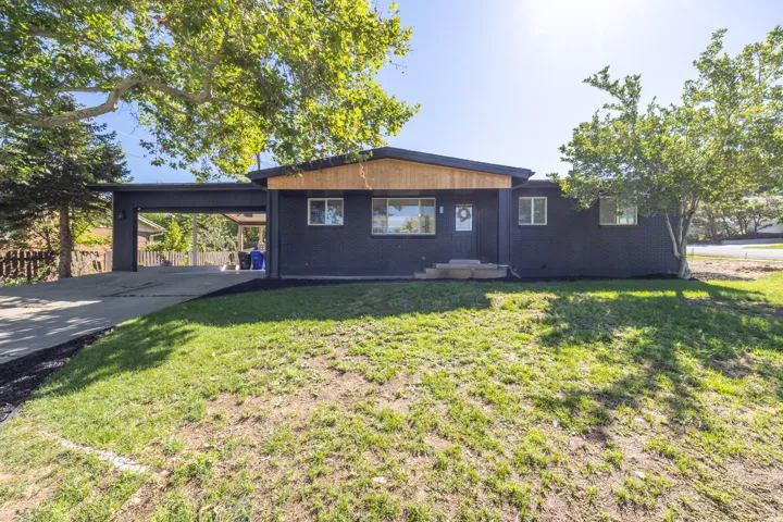 Contemporary exterior with dark siding and natural wood paneling, featuring a covered carport and a sloped roofline