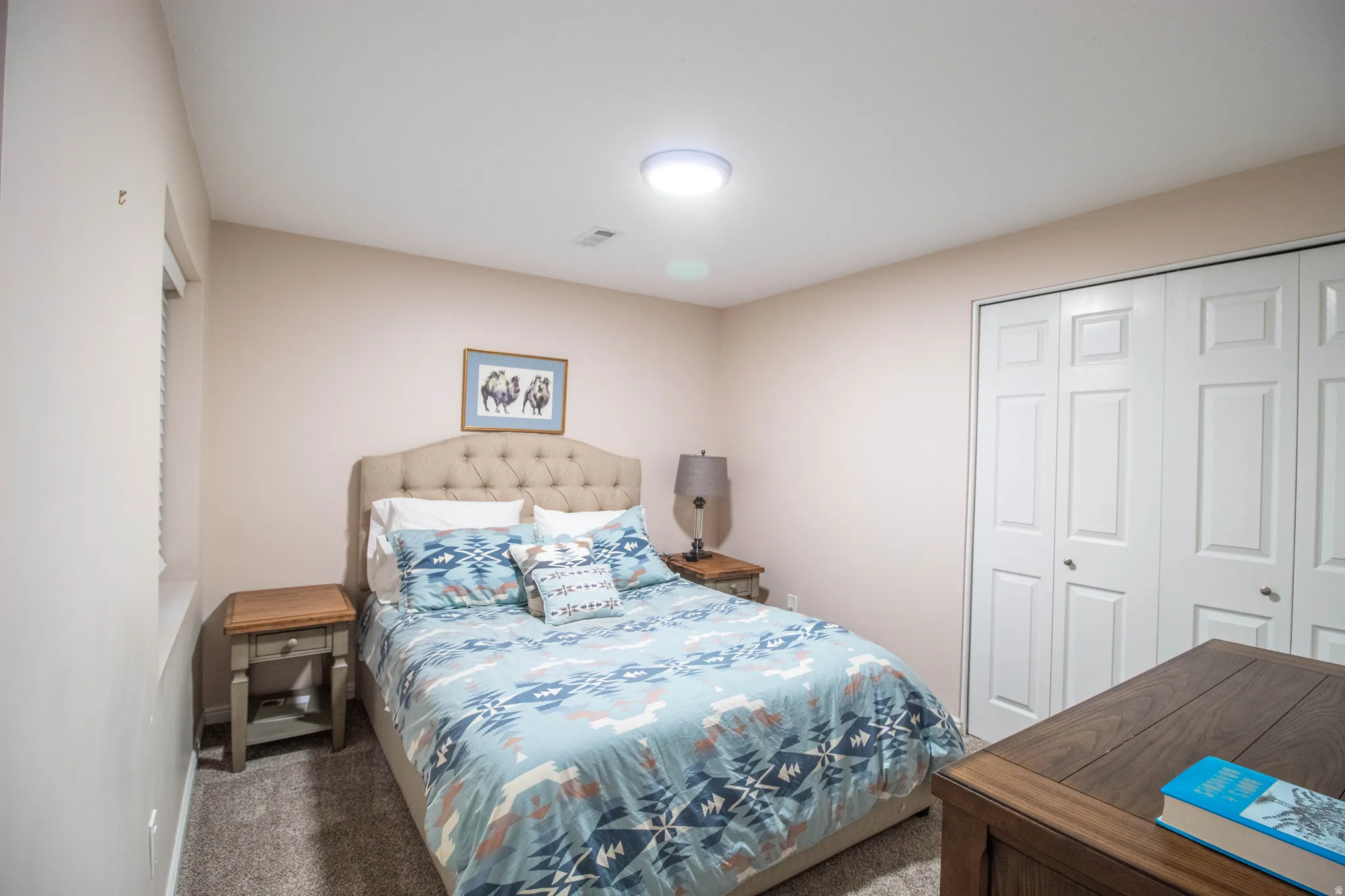 Carpeted flooring with light-toned walls, featuring a window and white bi-fold closet doors