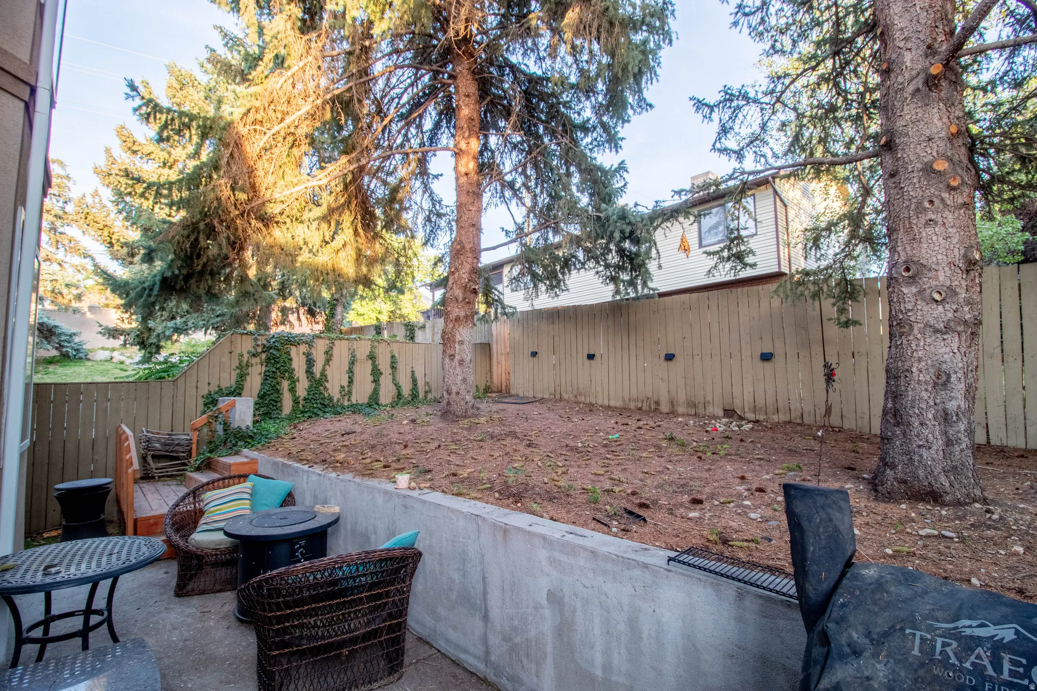 Concrete patio with a retaining wall, wood fence perimeter, and mature trees