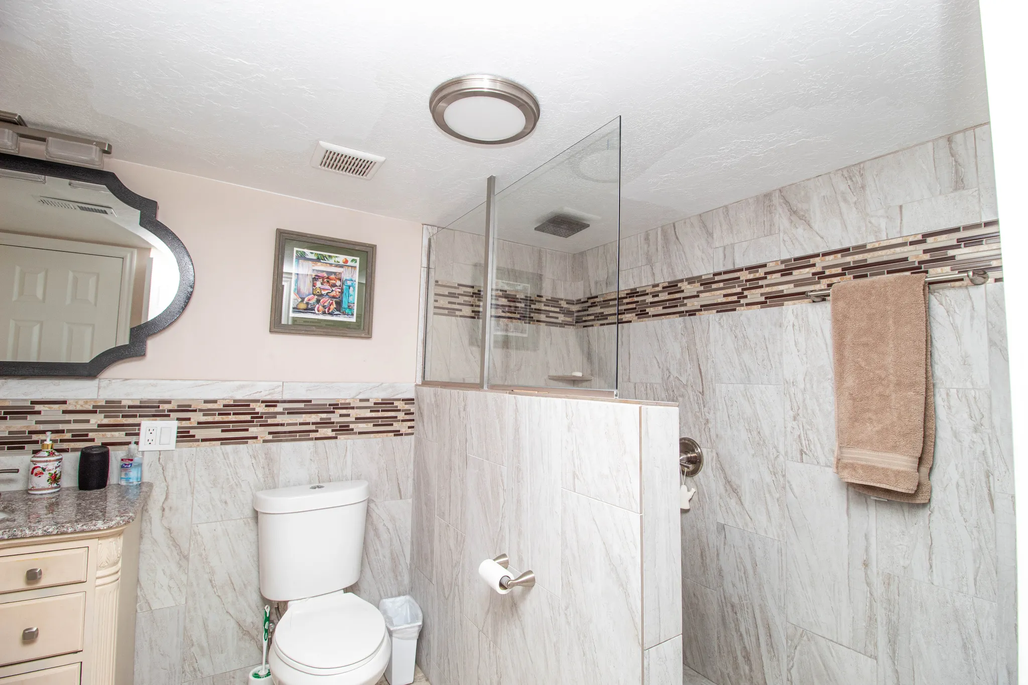 Walk-in shower with glass partition and tile surround, complemented by a decorative tile accent band and recessed lighting