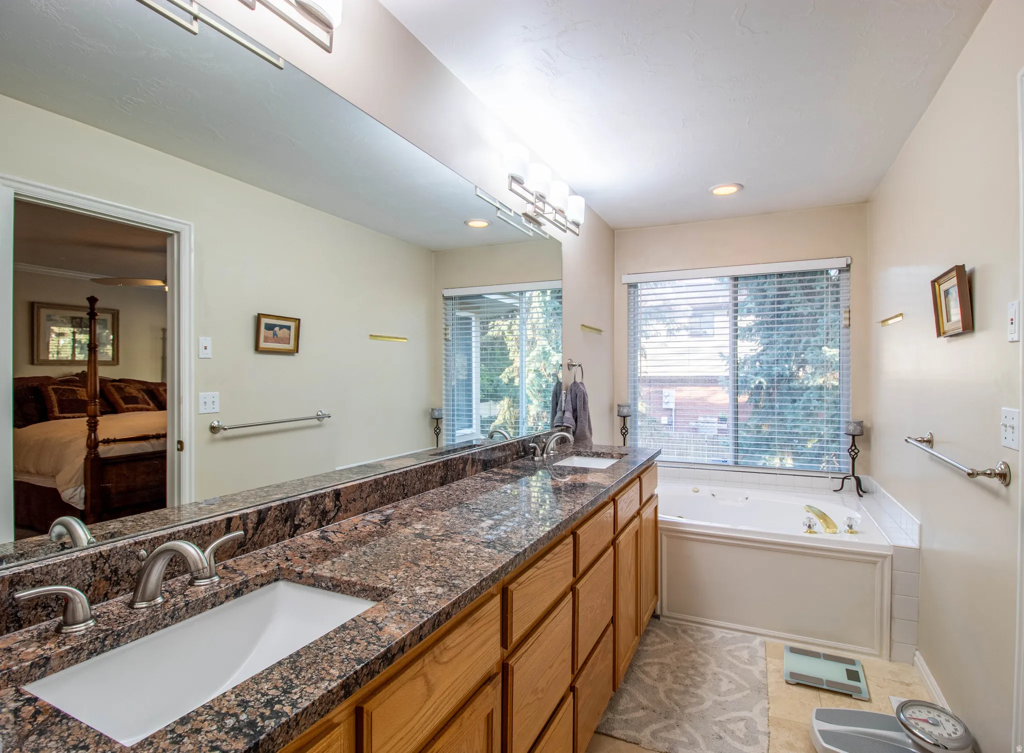 Dual vanity with integrated sinks, expansive counter space with a stone-finish surface, wood-finish cabinetry, and a built-in jetted tub
