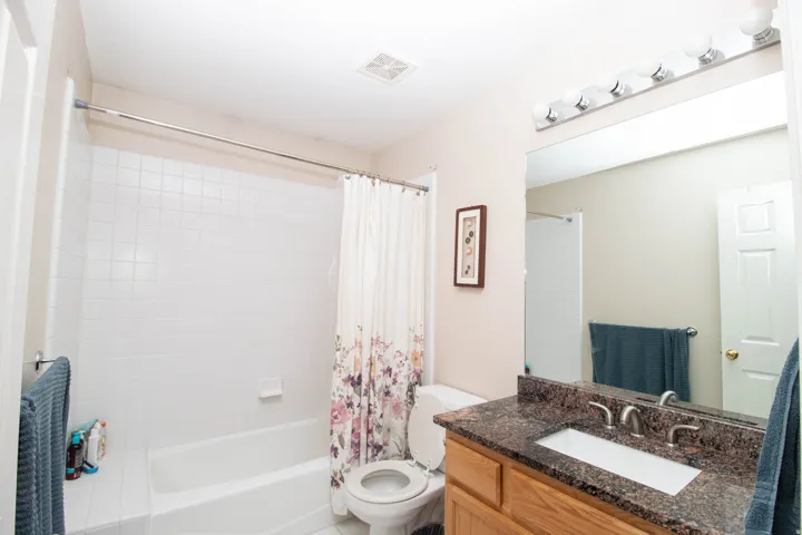Bathtub with white subway tile surround, integrated vanity with a rectangular sink, dual-handle faucet, and granite-look countertop