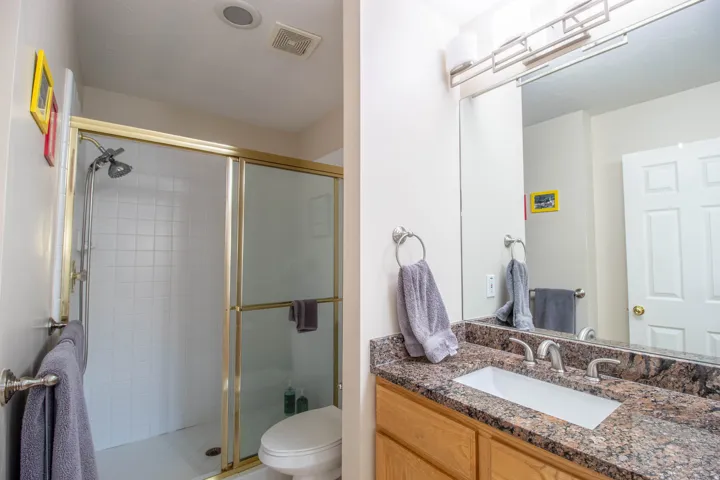Shower with gold-toned framed glass enclosure, white tiled walls, and a fixed showerhead