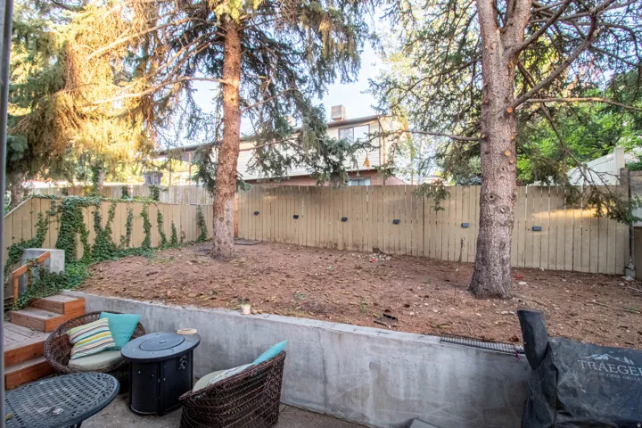 Private rear yard featuring a wood fence, mature trees, and a concrete retaining wall