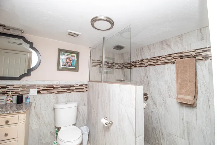 Walk-in shower with glass partition and tile surround, complemented by a decorative tile accent band and recessed lighting
