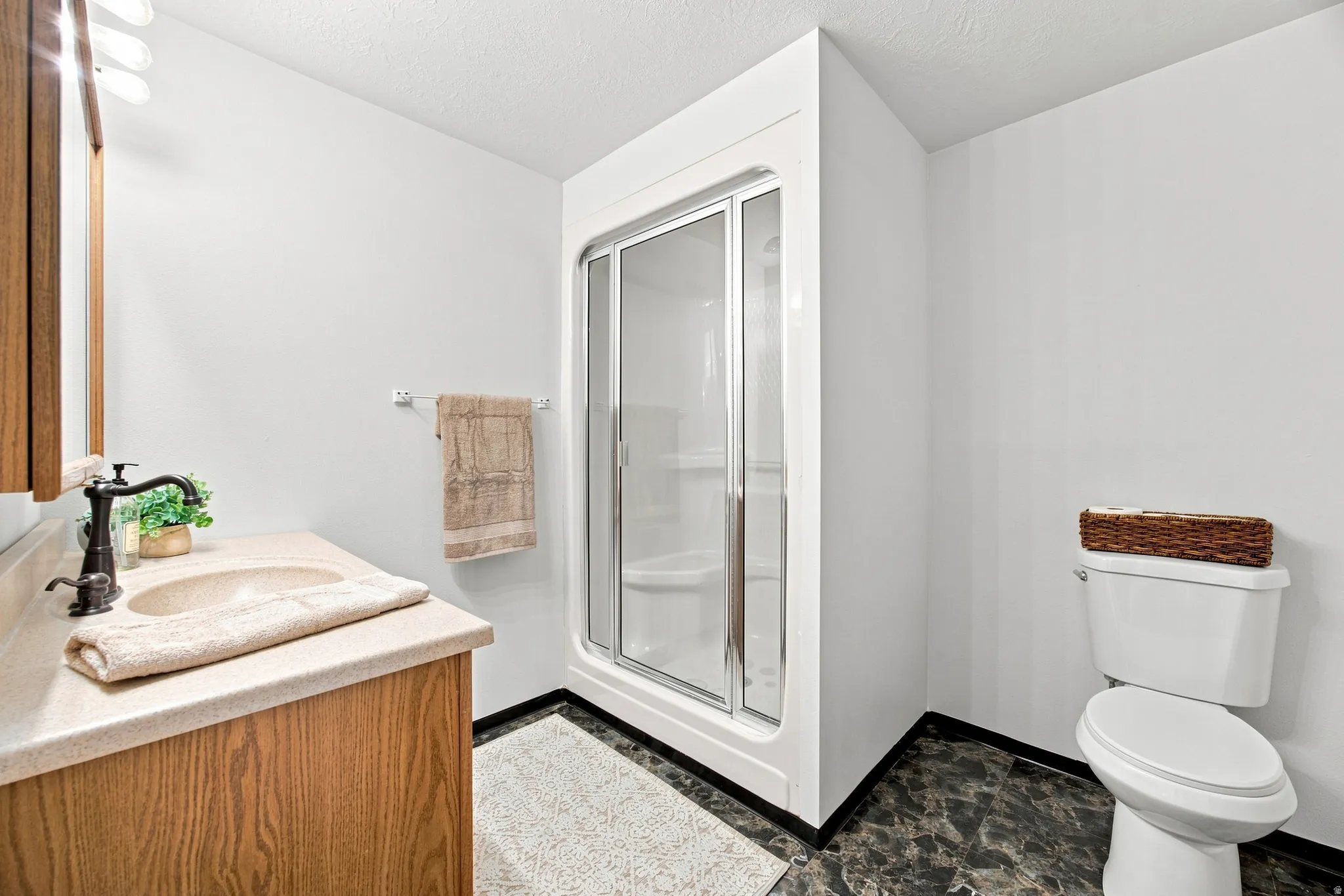Bathroom featuring a wood-finish vanity with an integrated sink, a shower enclosure with sliding glass doors, and dark marble-look flooring