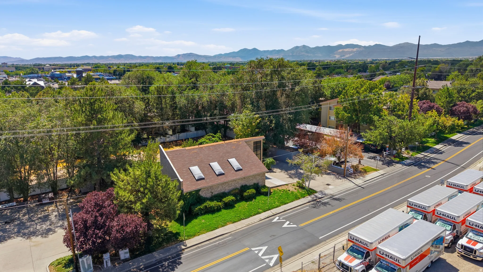 Gabled roofline with multiple skylights, stone-clad exterior, established landscaping, and paved surface parking