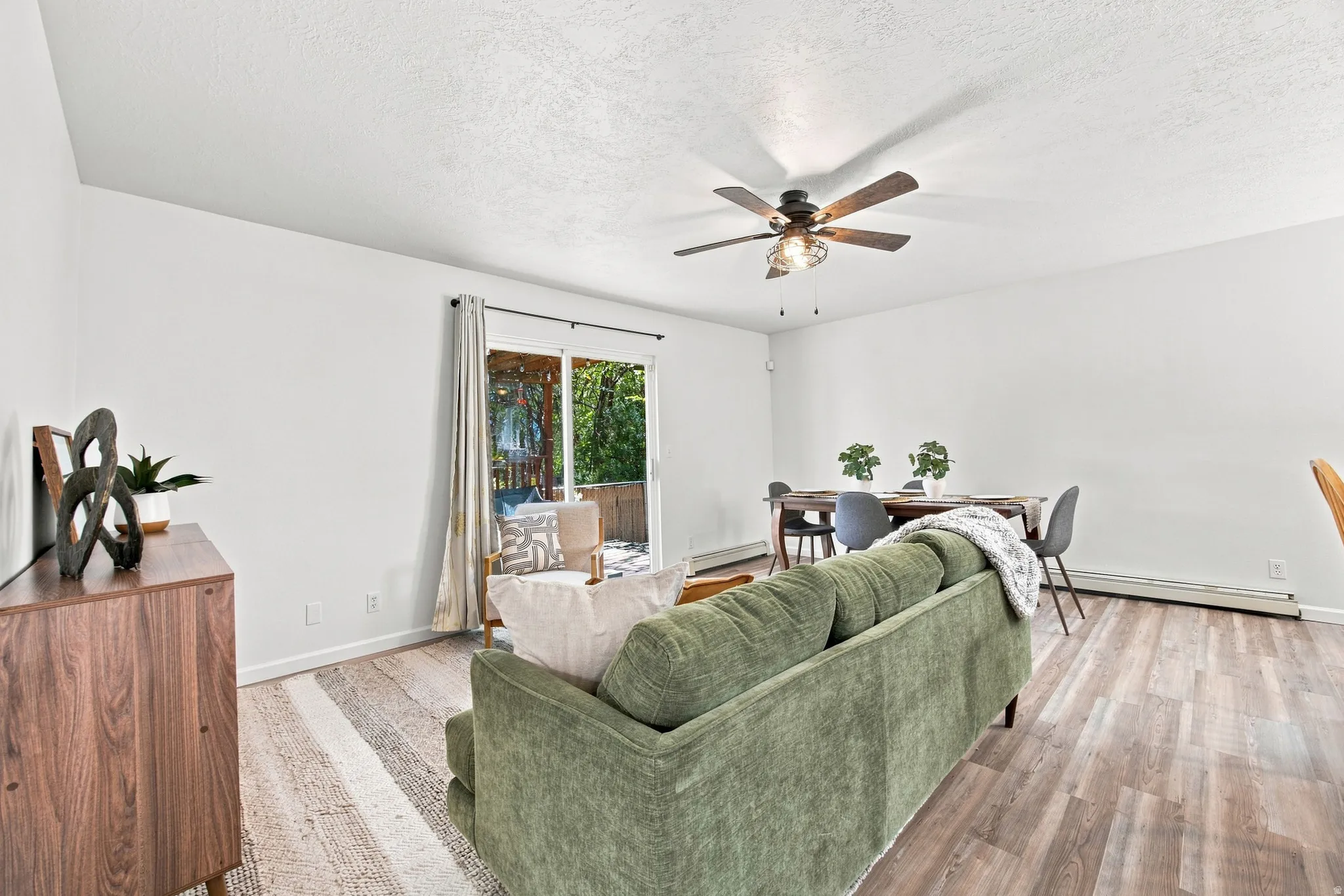 Wood-finish flooring throughout, bright white walls, sliding glass door, and a ceiling fan with integrated lighting