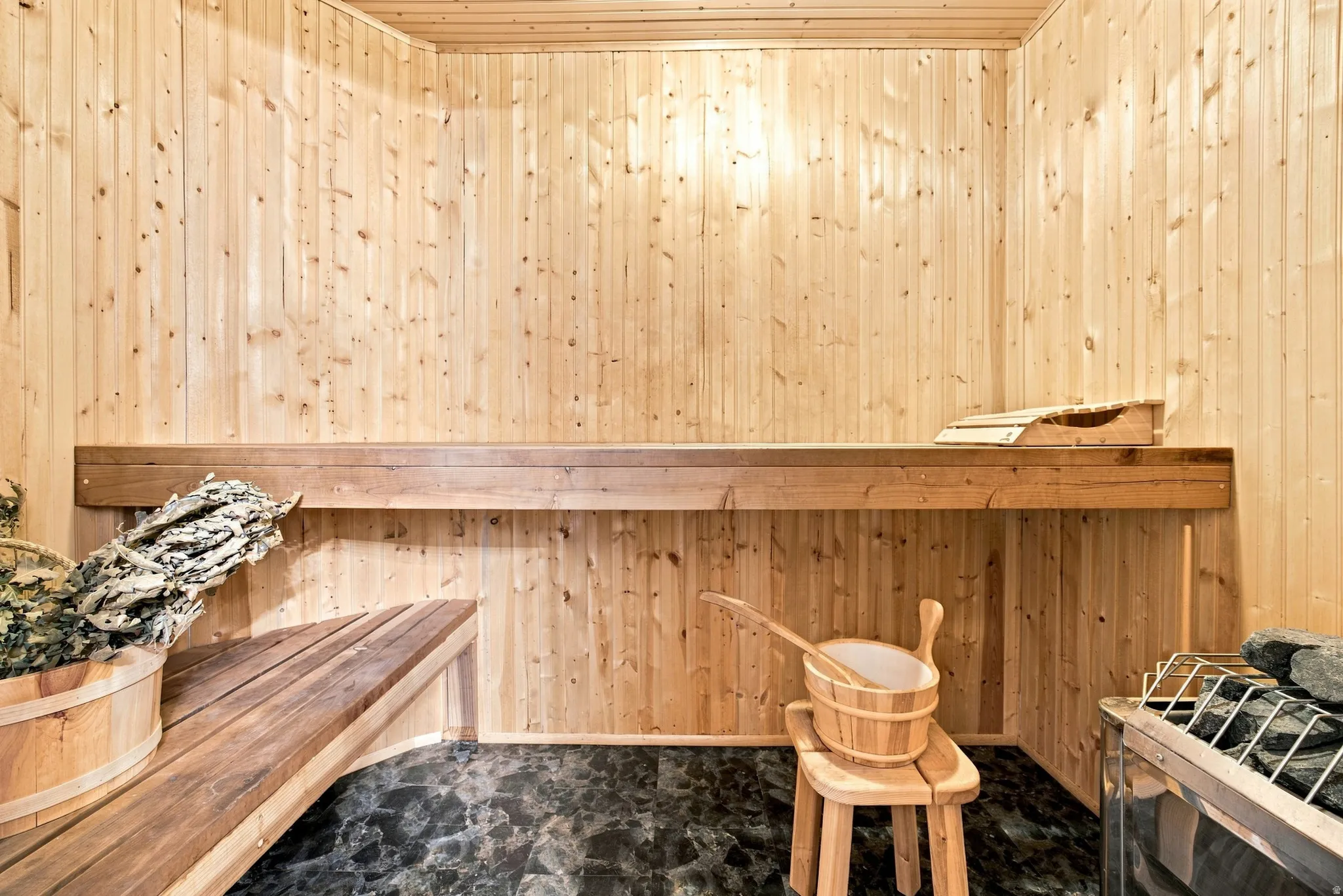 Wood-paneled sauna featuring built-in wooden benches and dark stone flooring