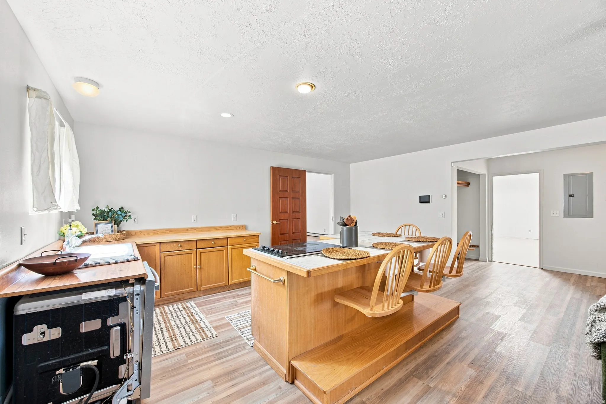 Wood-finish flooring throughout, kitchen island with integrated cooktop, natural wood cabinetry, and recessed lighting