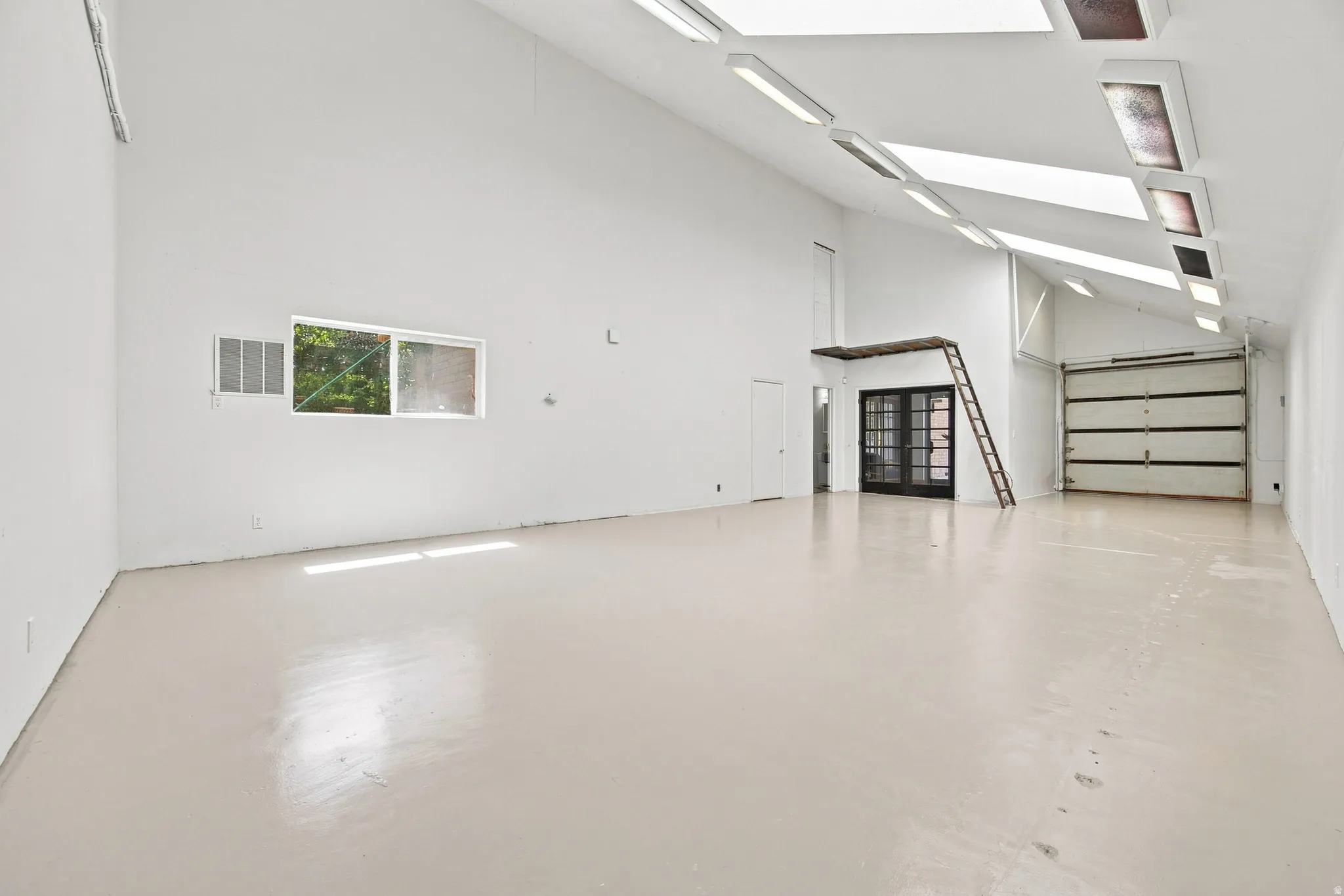 Expansive open space with vaulted ceilings, multiple skylights, a large roll-up door, and a mezzanine structure