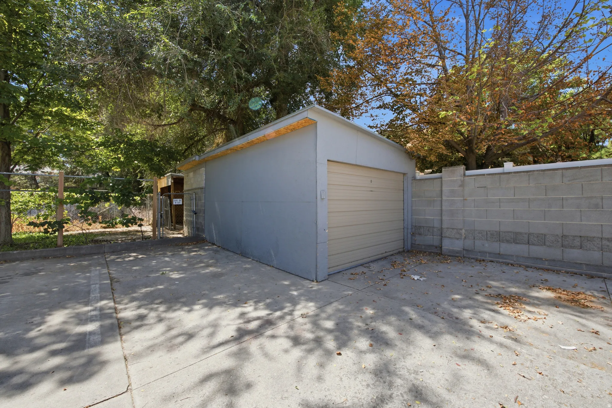 Detached garage with a roll-up door, paved parking area, and concrete block perimeter wall