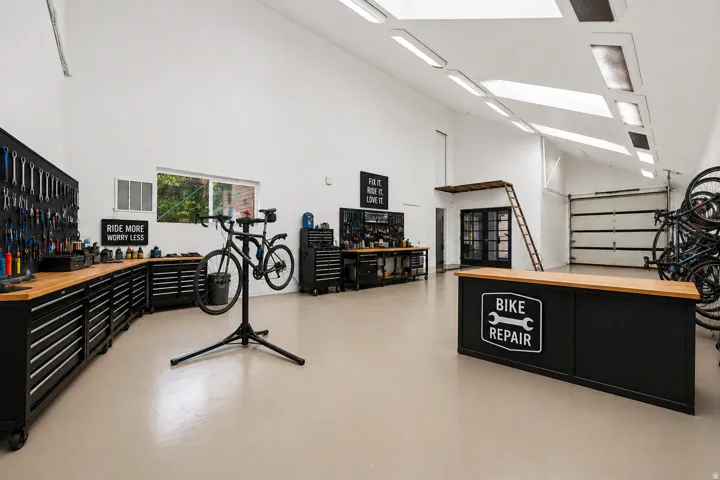 Spacious utility area with high ceilings, multiple skylights, dedicated workbench with storage, roll-up garage door, and a built-in mezzanine