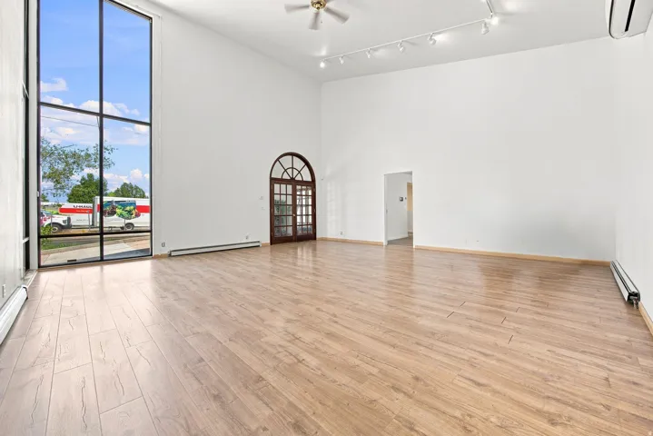 Vaulted ceiling with track lighting, wood-finish flooring, two-story window, arched double door, and wall-mounted air conditioning unit