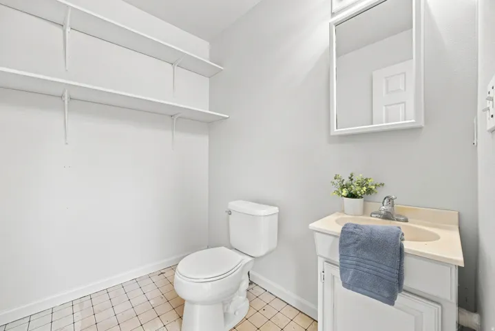 White vanity with integrated sink, wall-mounted mirror, and tile flooring