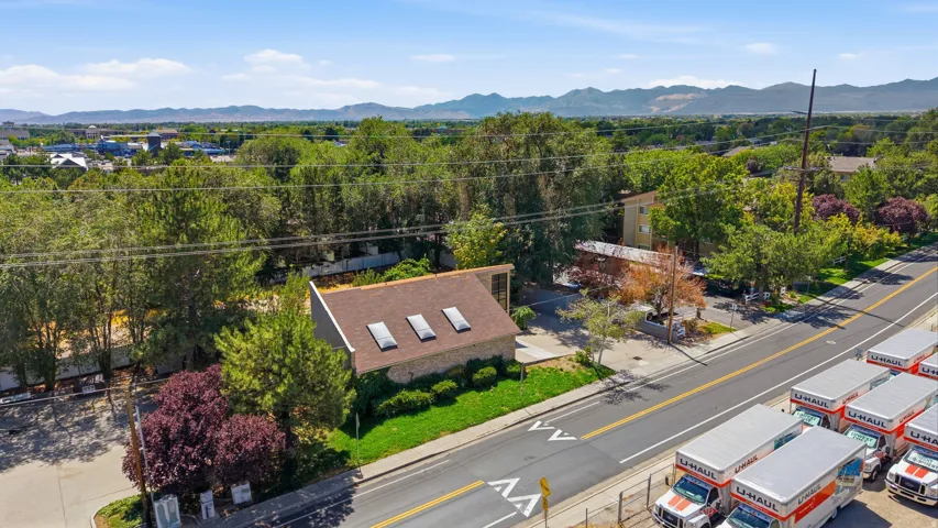 Gabled roofline with multiple skylights, stone-clad exterior, established landscaping, and paved surface parking