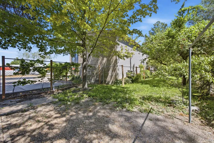 Expansive outdoor space featuring mature trees, a chain-link fence, and a gravel ground covering