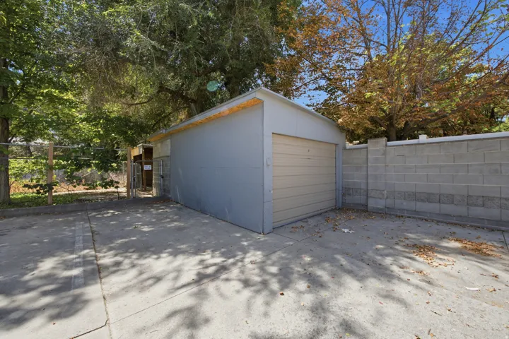 Detached garage with a roll-up door, paved parking area, and concrete block perimeter wall