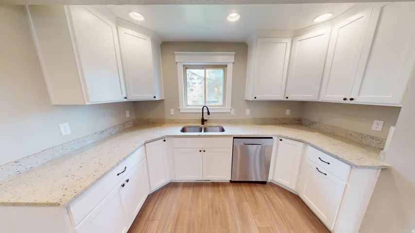 U-shaped kitchen featuring white shaker cabinetry, speckled countertops, wood-finish flooring, and a stainless steel dishwasher