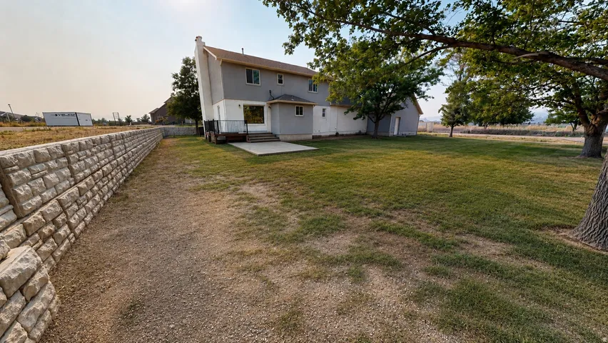 This is an Ai enhanced Photo. Expansive lawn area with mature trees, a durable stone retaining wall, and a concrete patio