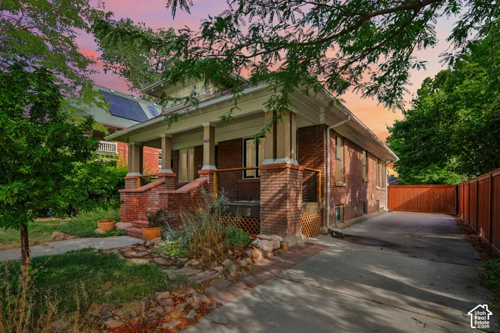 Brick exterior featuring a covered porch with column supports, a private driveway, and a wood fence