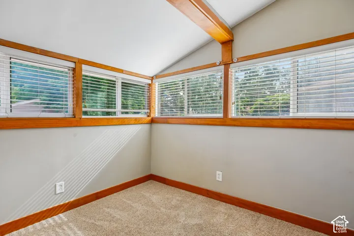 Vaulted ceiling with exposed wood beams, wood-frame windows with horizontal blinds, and neutral carpet flooring