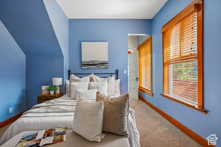 Sloped ceiling design, wood-finish window frames, wood-finish blinds, wood-finish trim, and carpeted flooring