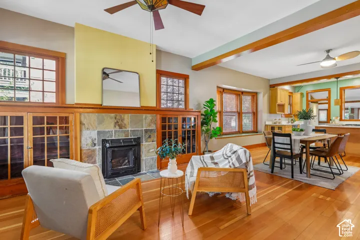 Hardwood flooring throughout, stone-tiled fireplace with a black insert, built-in wooden cabinetry, wooden window framing, and exposed wooden beams