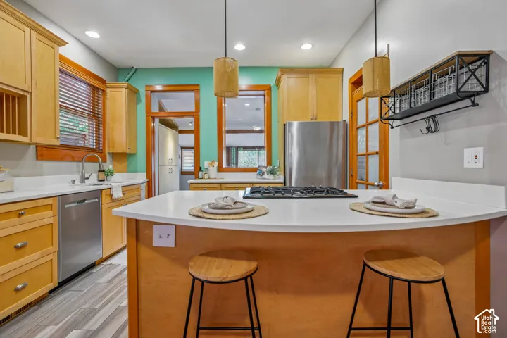 Kitchen featuring wood cabinetry, stainless steel appliances, a center island with countertop seating, white countertops, and wood-finish flooring